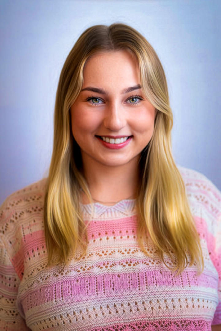 Headshot of a smiling blonde woman with green eyes, wearing a pastel pink and white sweater.