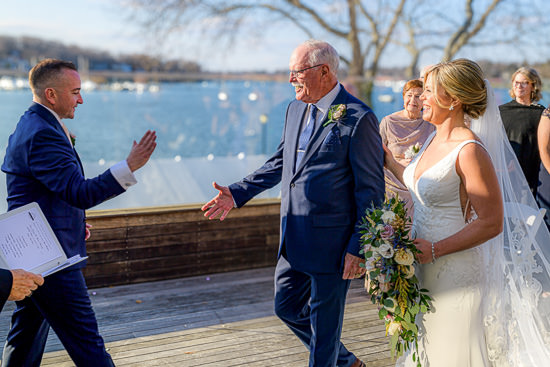 Bride and father meet groom at outdoor wedding ceremony.