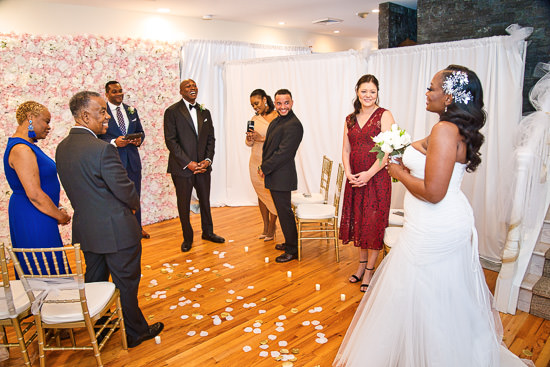 Bride at wedding ceremony with guests and flower wall.