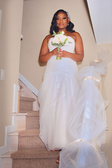 Bride in white dress on stairs with bouquet.