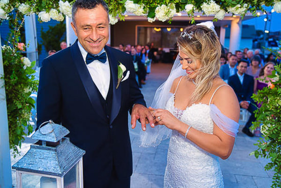 Bride places ring on groom's finger at outdoor wedding.