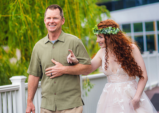Father walks bride, adorned with flower crown, down aisle.