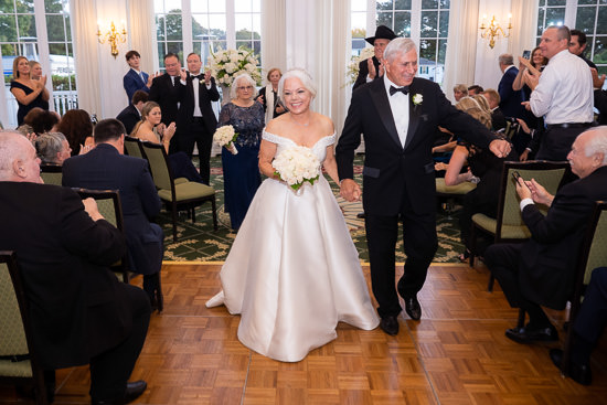 Mature couple's wedding reception grand entrance, applauded by guests.