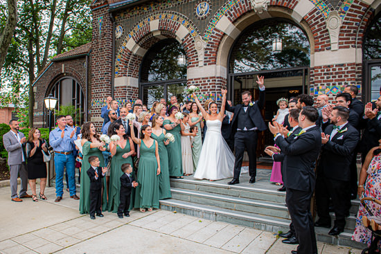 Newlyweds celebrated by wedding party outside ornate building.