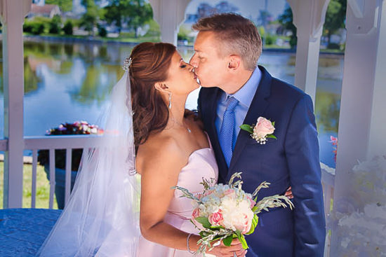 Newlyweds share a kiss in a gazebo by the water.