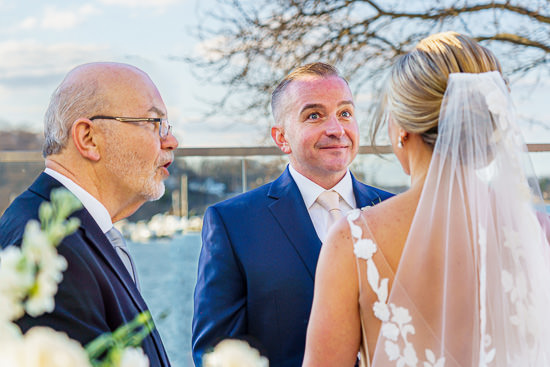 Wedding ceremony by the water with officiant and couple.