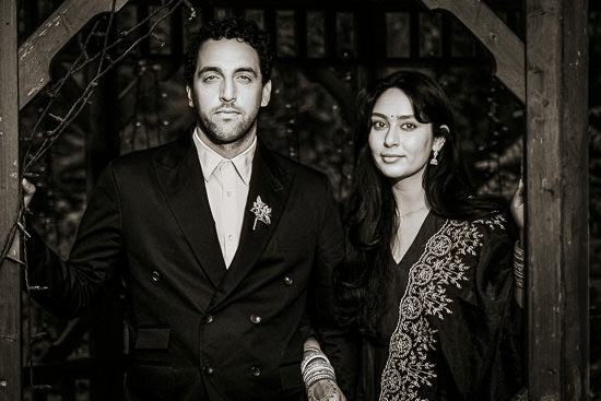 Black and white photo of a couple standing in a doorway the man wears a suit and the woman wears traditional indian clothing they are both looking at the camera
